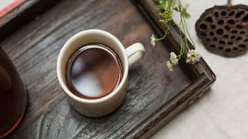 A white cup of tea on a wooden tray with a decorative item and a small plant.