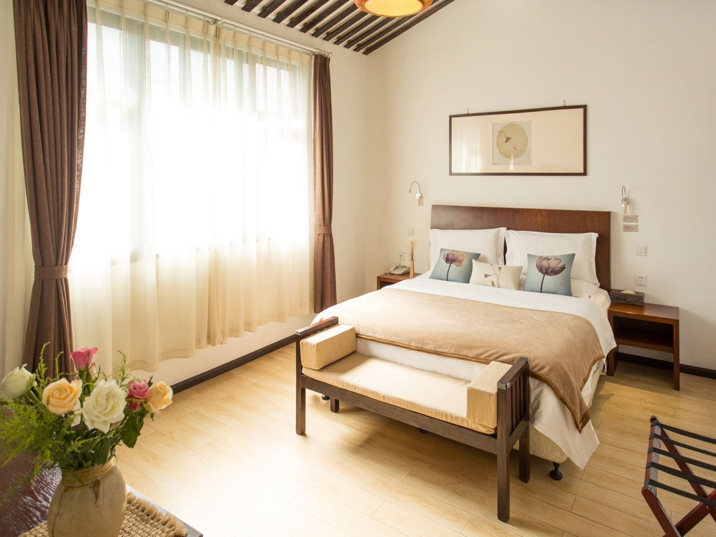 A bedroom with a wooden bed, a nightstand, a bedside table, a framed picture on the wall, and a window with curtains.