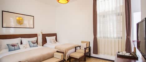 A hotel room with two beds, a wooden bench, a TV, and a large window with curtains.