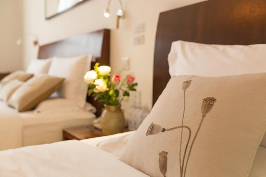 Un dormitorio ordenado con cama, almohadas y un florero con flores.