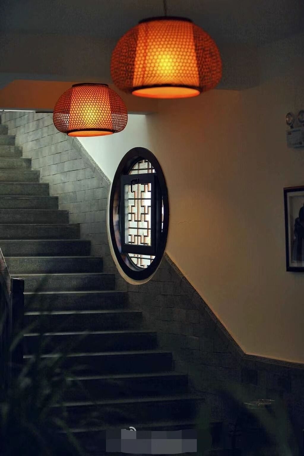 A staircase with a geometric patterned window and two hanging lamps.