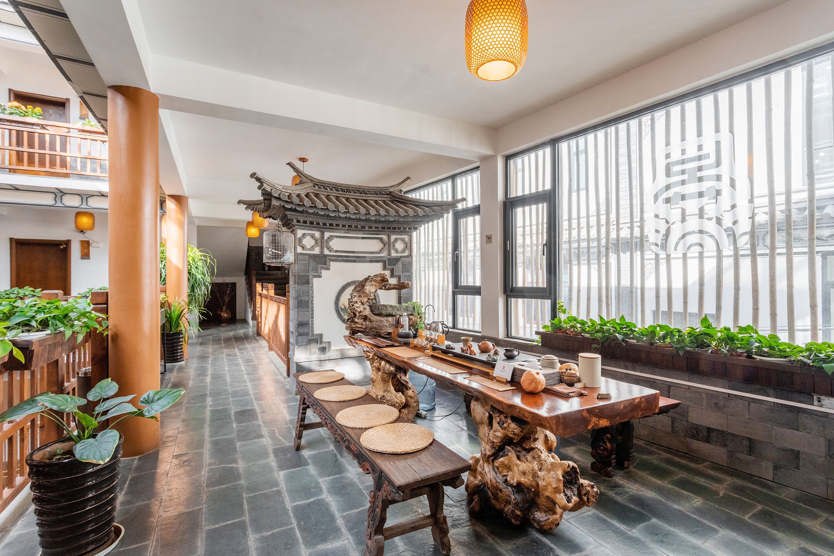 A traditional-style interior with a long wooden table, potted plants, and a decorative ceiling structure.