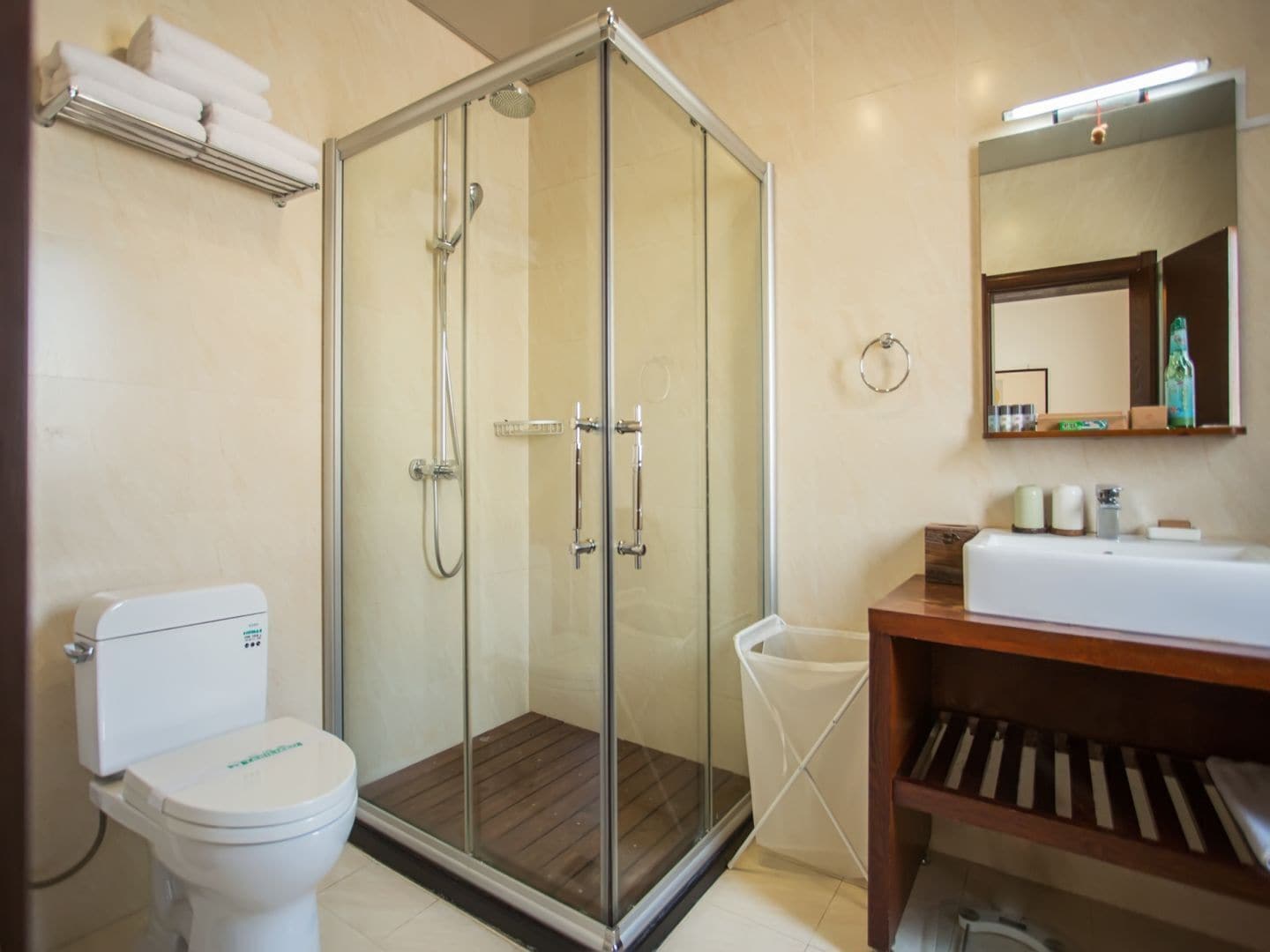 A modern bathroom with a glass-enclosed shower, a white toilet, a wooden vanity with a mirror, and a towel rack above the toilet.