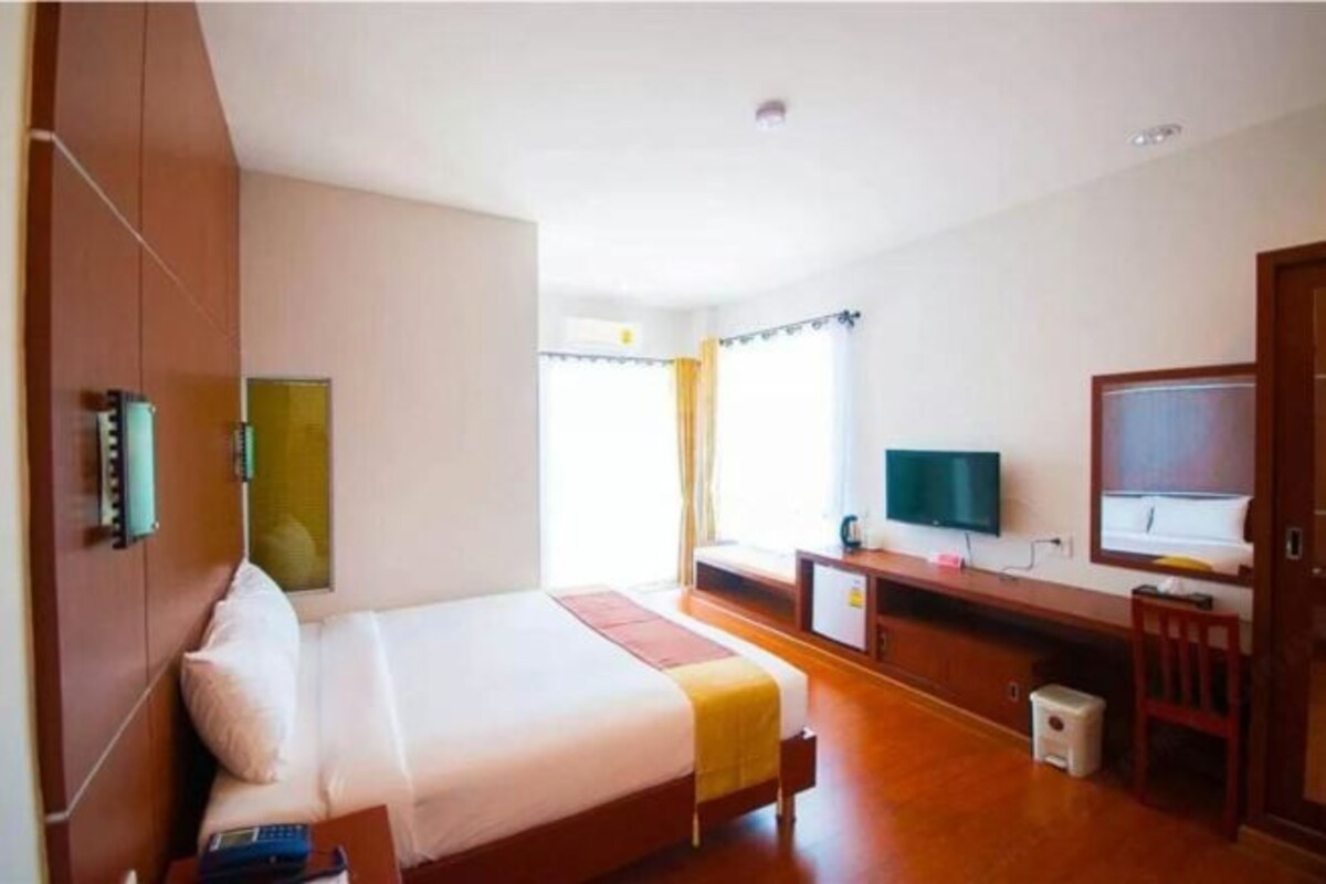 A hotel room with a bed, a desk, a television, and a window with curtains.
