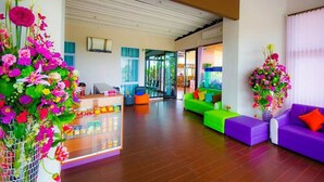Un moderno vestíbulo de hotel con un mostrador de recepción, sofás coloridos y grandes arreglos florales.