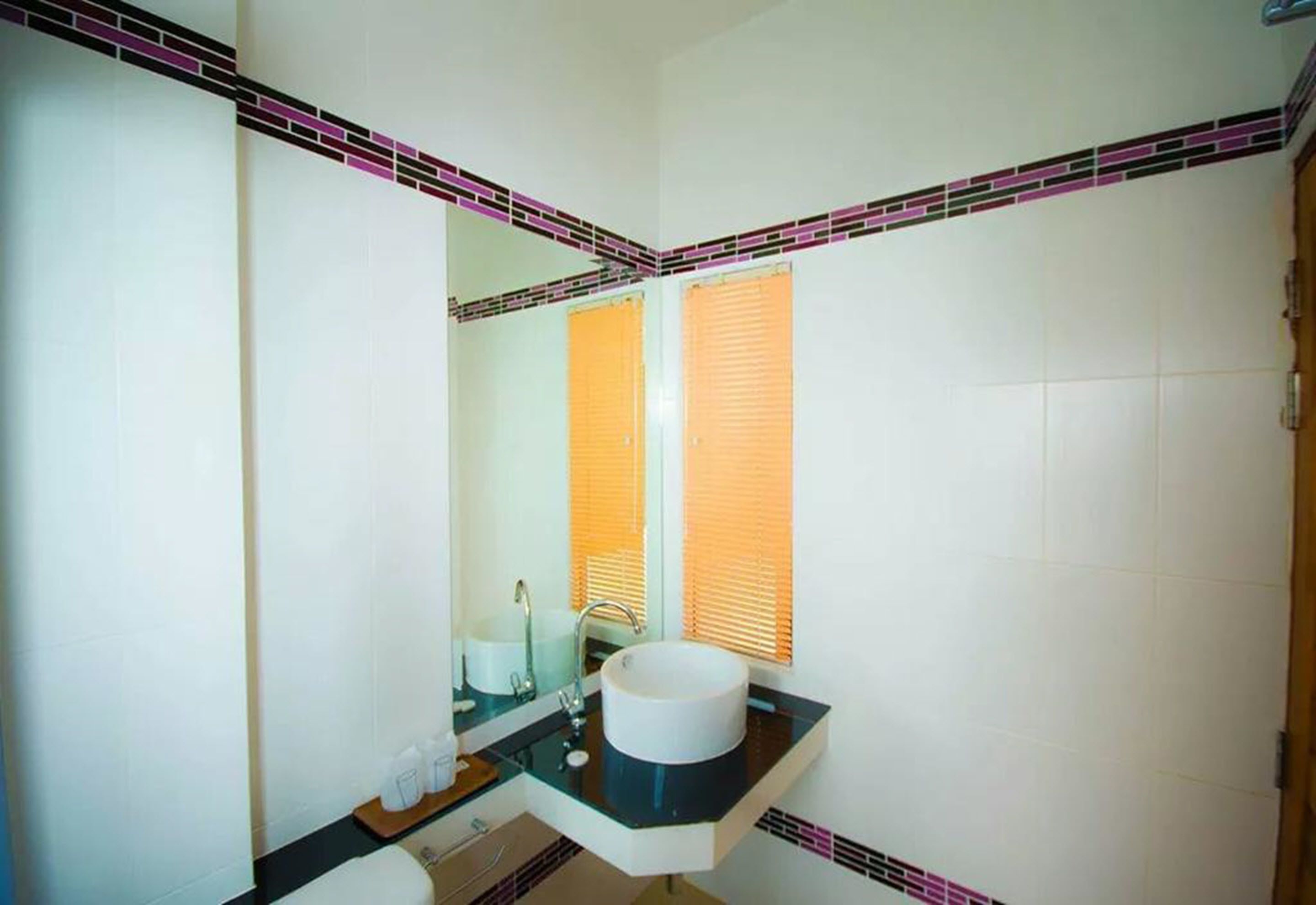 Een badkamer met een wit wastafelmeubel, een spiegel en een raam met zonwering.