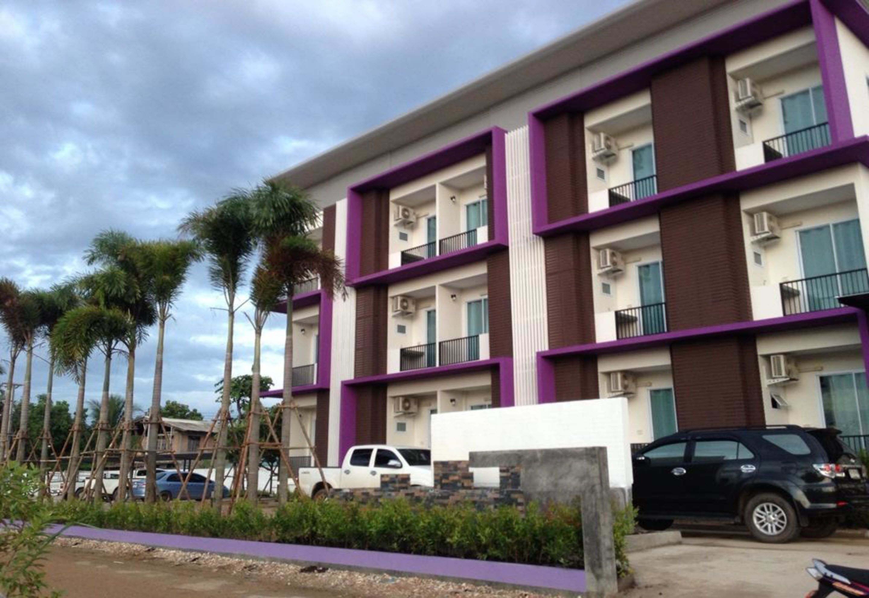 Een meerhoog hotel met balkons, geparkeerde auto's en palmbomen.