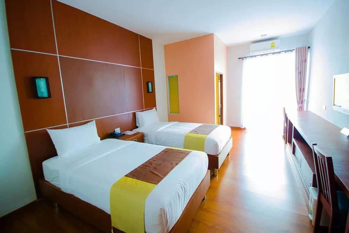 A hotel room with two beds, a wooden headboard, a desk, and a window with curtains.