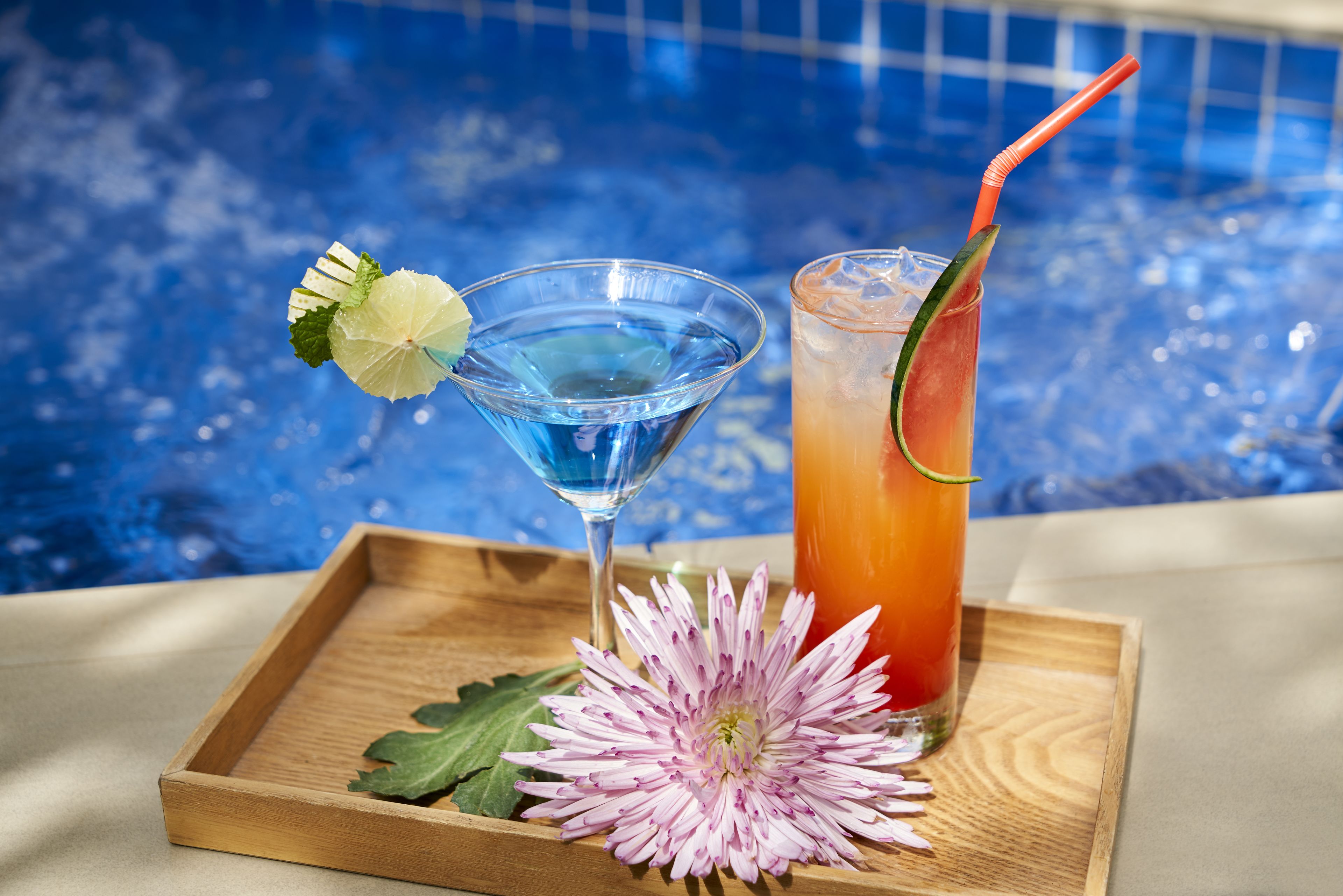 Deux boissons sur un plateau, avec une piscine en arrière-plan.