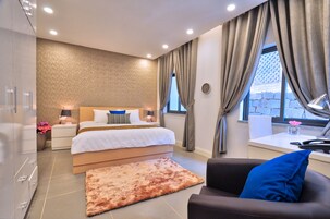 A modern bedroom with a large bed, bedside lamps, a nightstand, a desk, and a view of the outside.