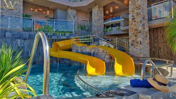 A pool area with a yellow water slide, stone walls, and a glass railing.