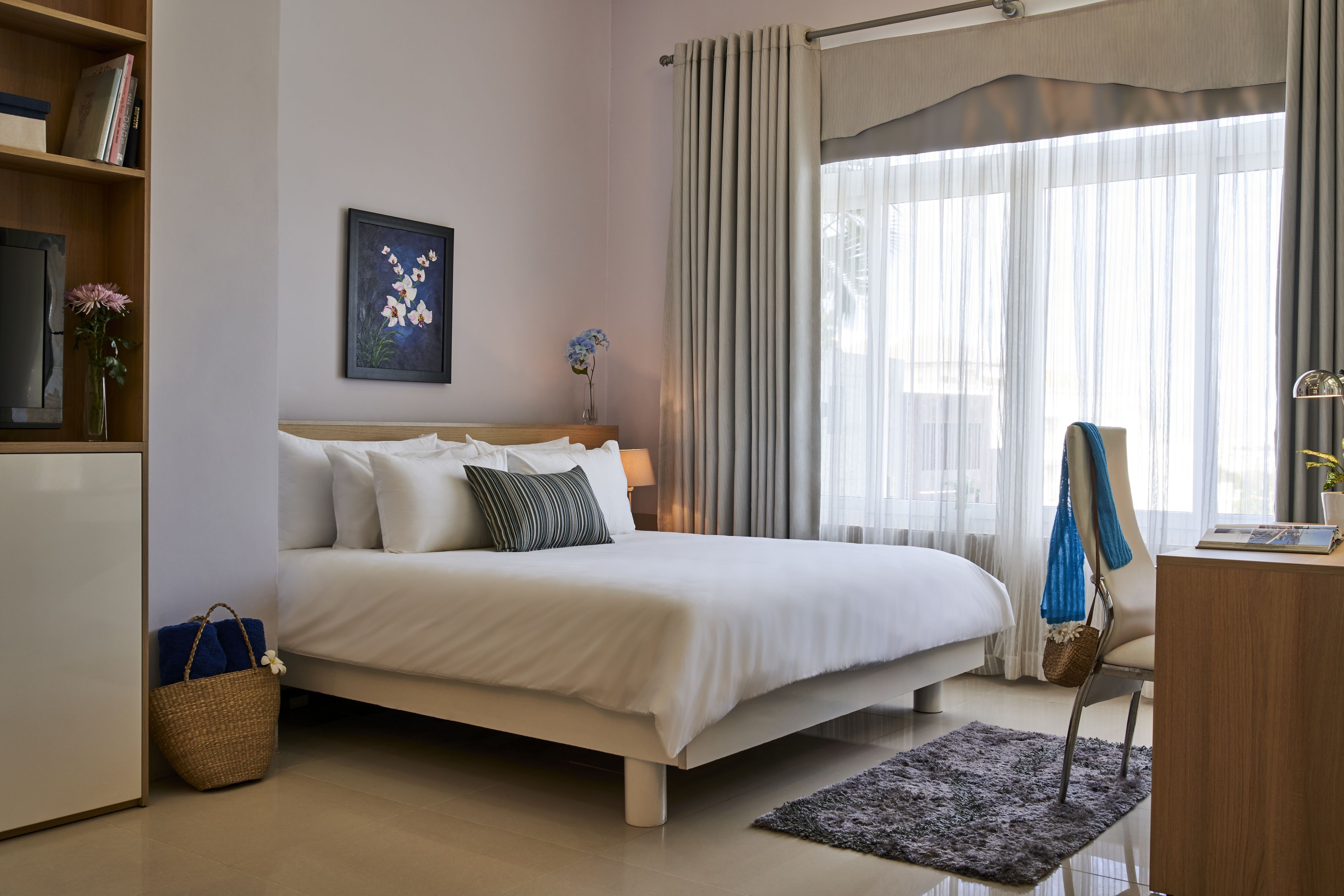 A neatly arranged bedroom with a bed, bedside table, lamp, and a window with curtains.