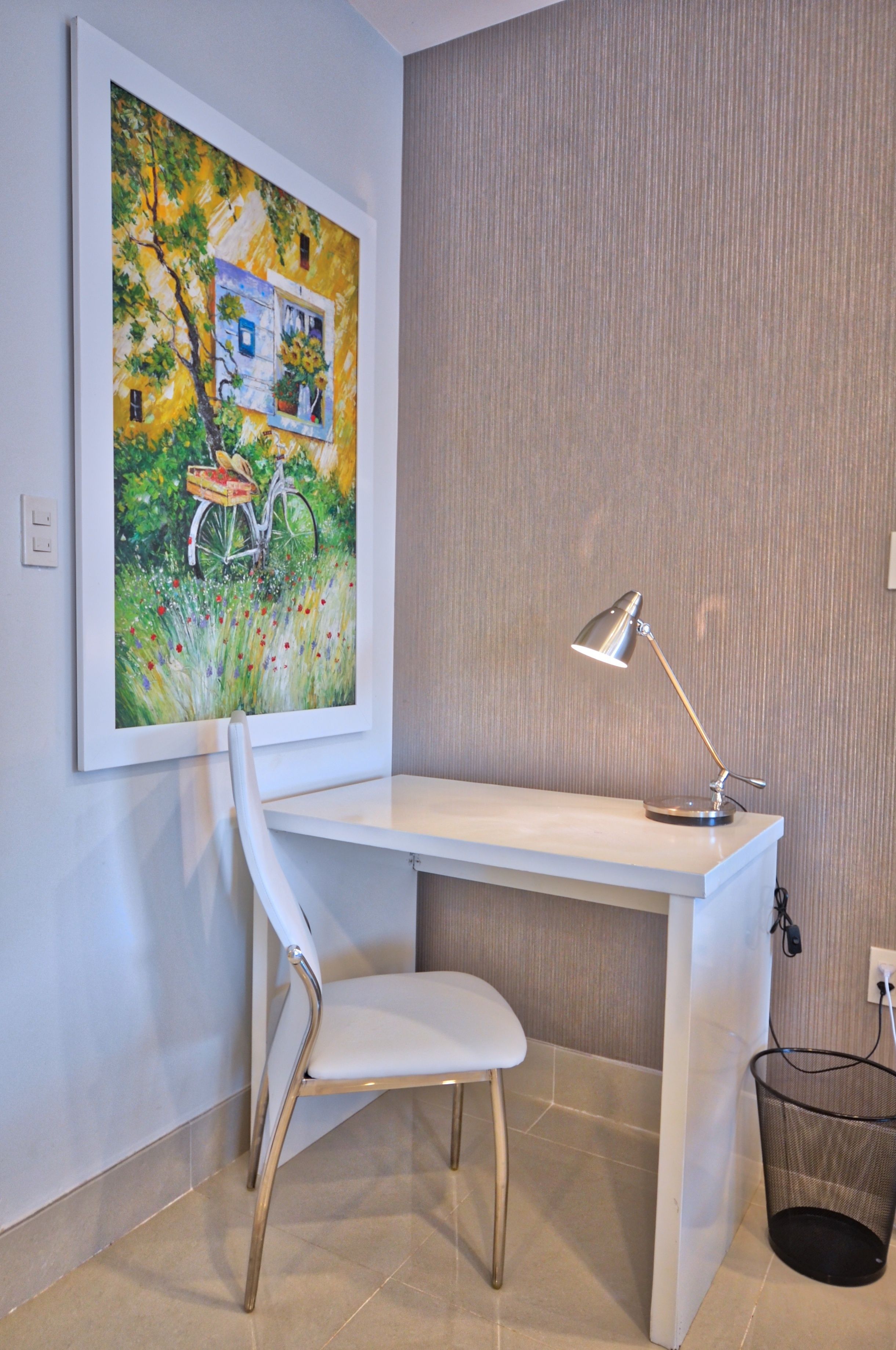 A modern office space with a white desk, a white chair, a framed painting, and a desk lamp.