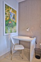 A modern office space with a white desk, a white chair, a framed painting, and a desk lamp.