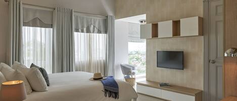 A modern bedroom with a large bed, a TV mounted on the wall, and a view of the outdoors.