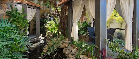 Un jardín tranquilo con un pequeño estanque, muros de piedra y una zona de estar cubierta.