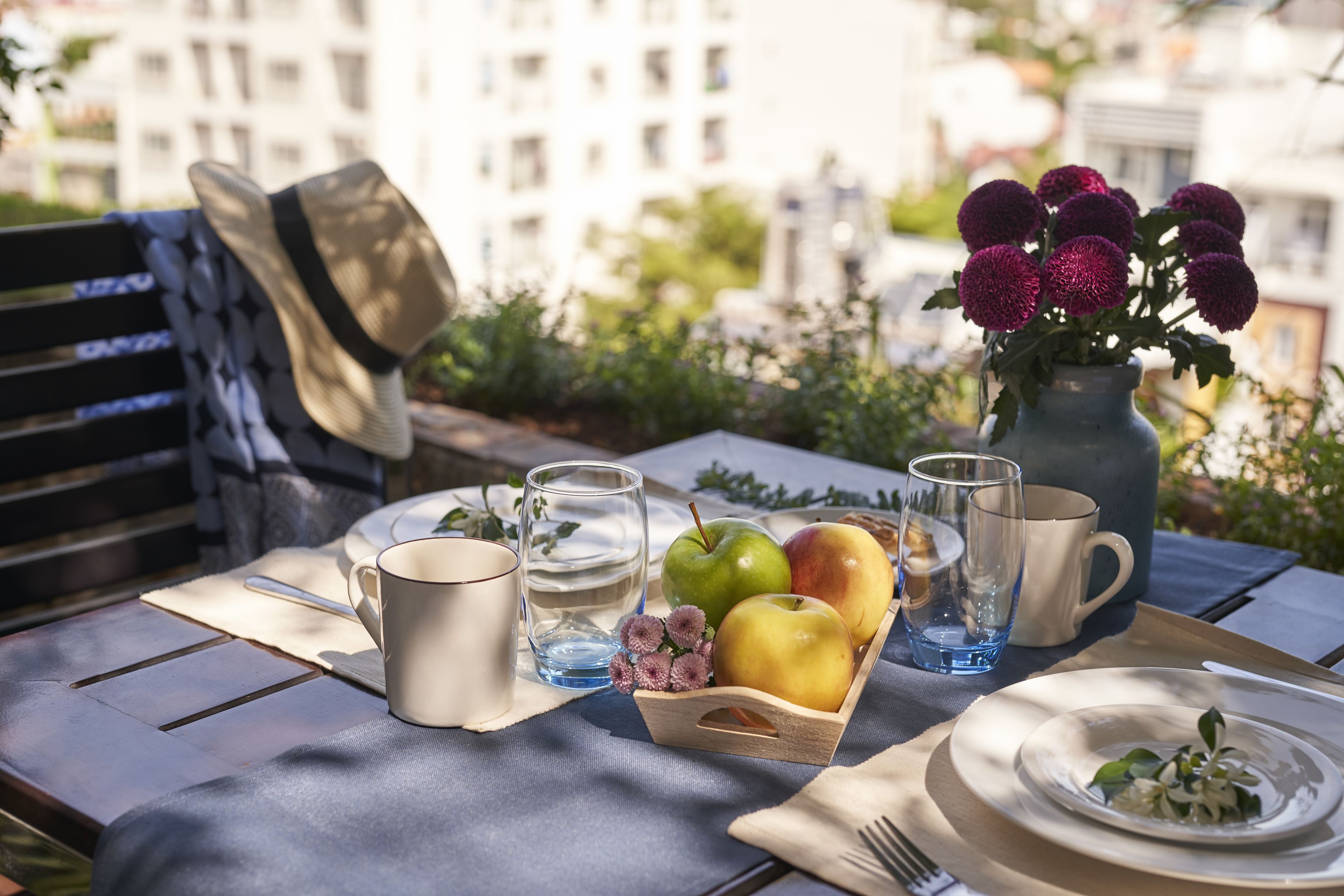 A table set with a hat, a vase with flowers, a fruit basket, and a plate with a fork.