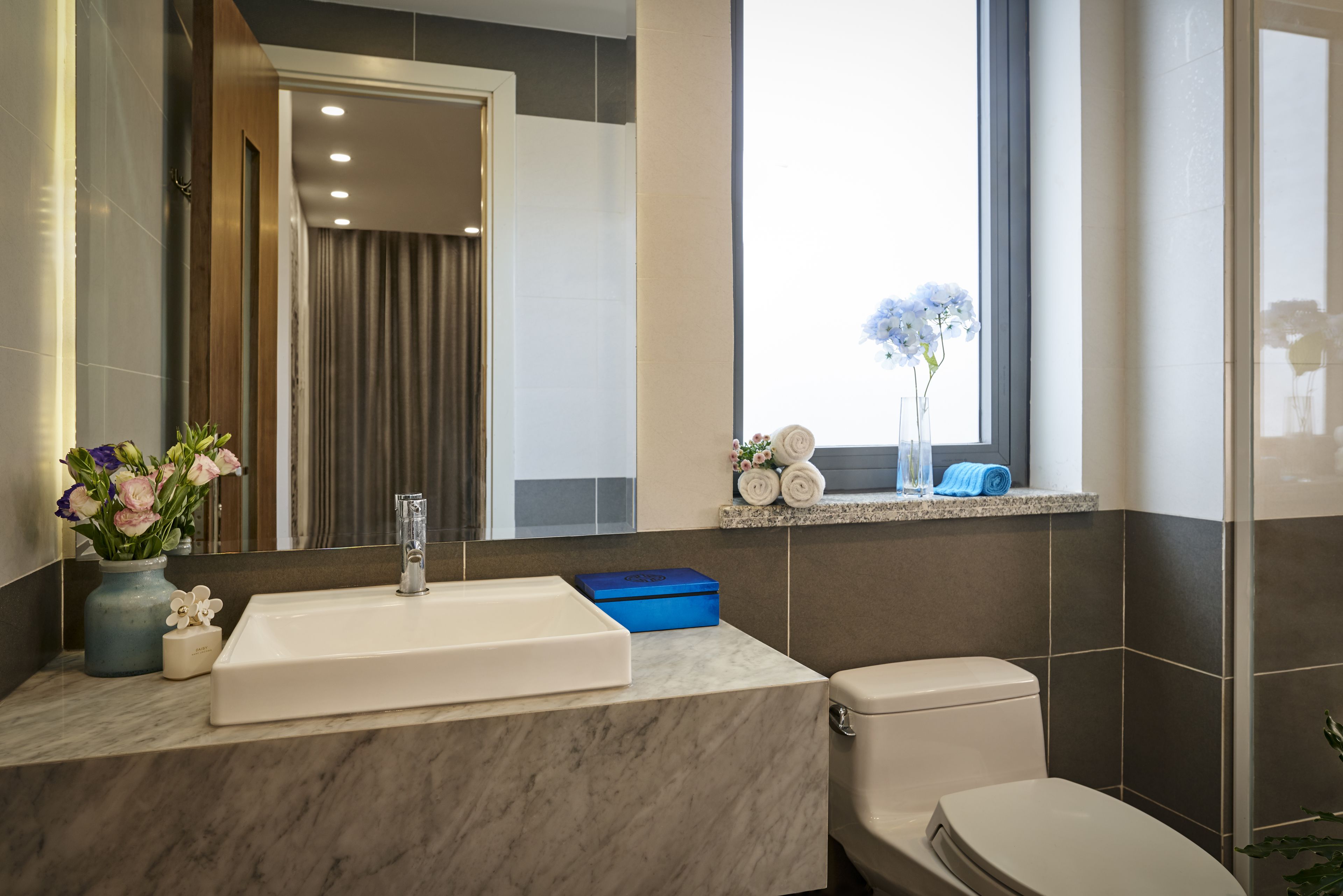 Een moderne badkamer met een marmeren wastafel, toilet en een raam met uitzicht.