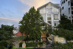 A boutique hotel with a prominent sign, a staircase leading to the entrance, and lush greenery surrounding the property.