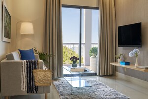 A modern living room with a sofa, a coffee table, a TV mounted on the wall, and a balcony with a view.