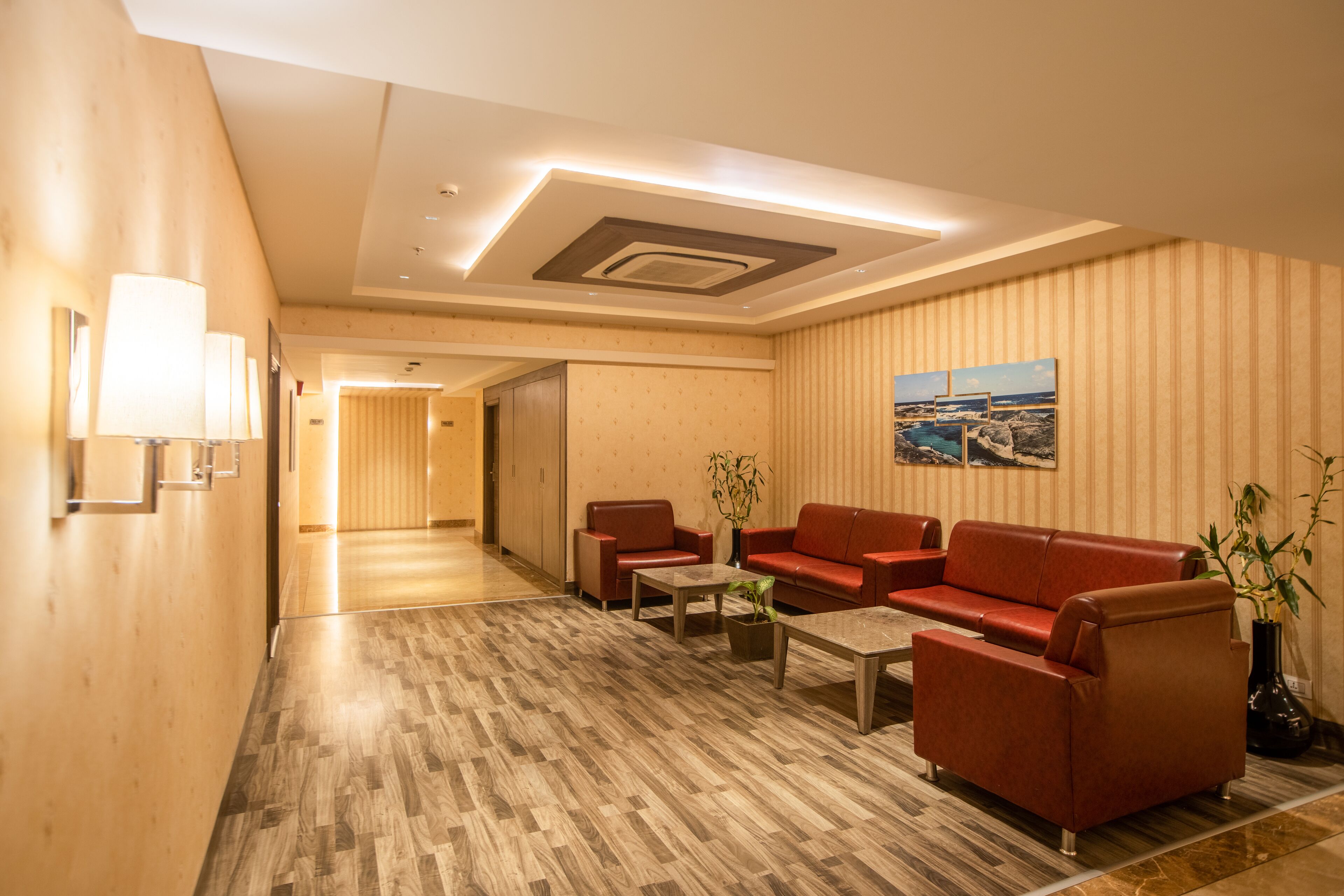 Un moderno hall de hotel con suelo de madera, sofás de cuero rojo, una mesa de centro y una lámpara de pared.