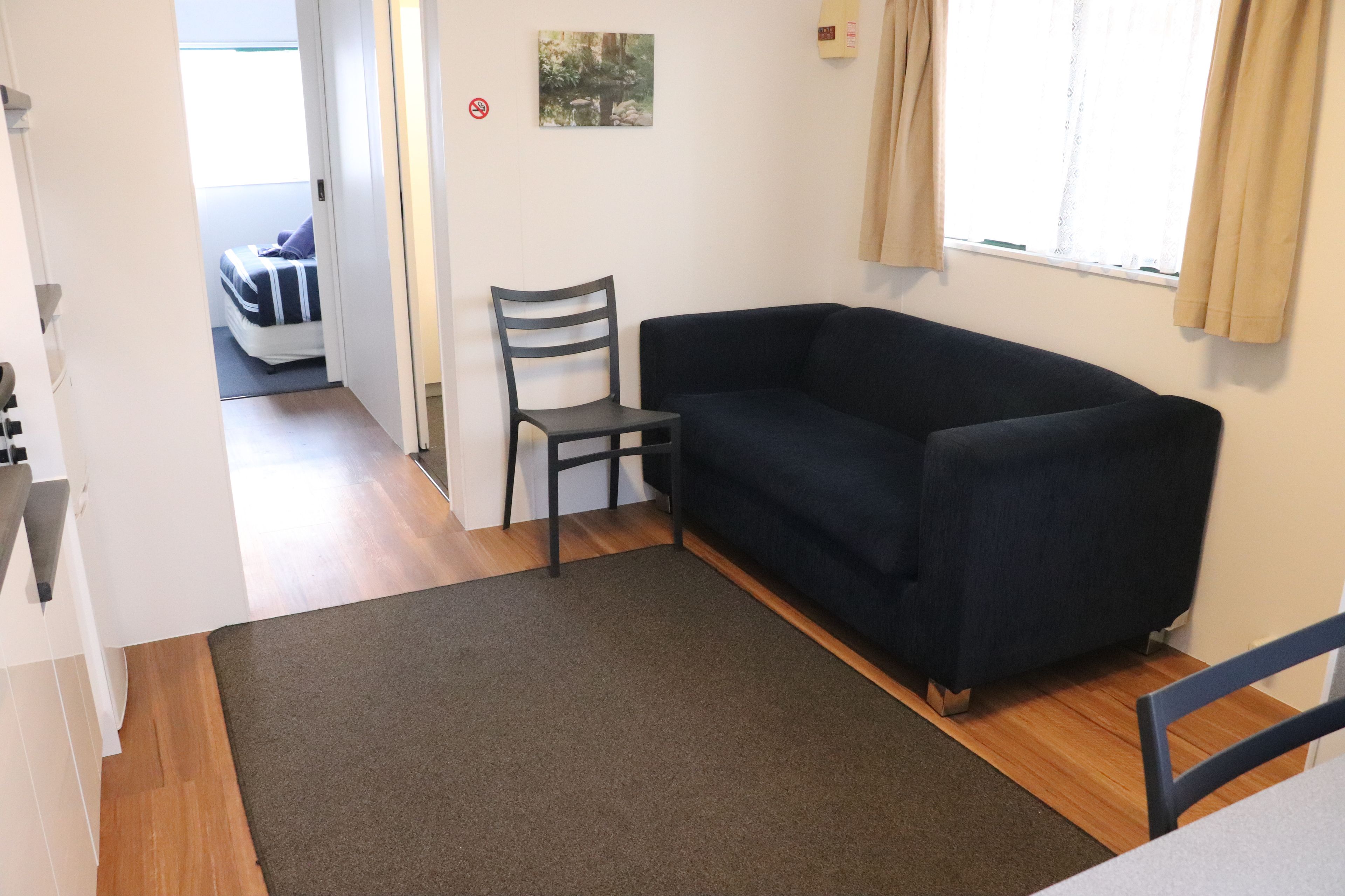 A room with a dark blue sofa, a grey chair, a small rug, and a bed in the background.