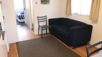 A room with a dark blue sofa, a grey chair, a small rug, and a bed in the background.