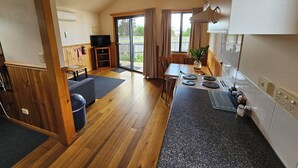 A compact kitchen with a stove, a dining table, and a TV. - Snug Beach Cabin And Caravan Park (Snug)