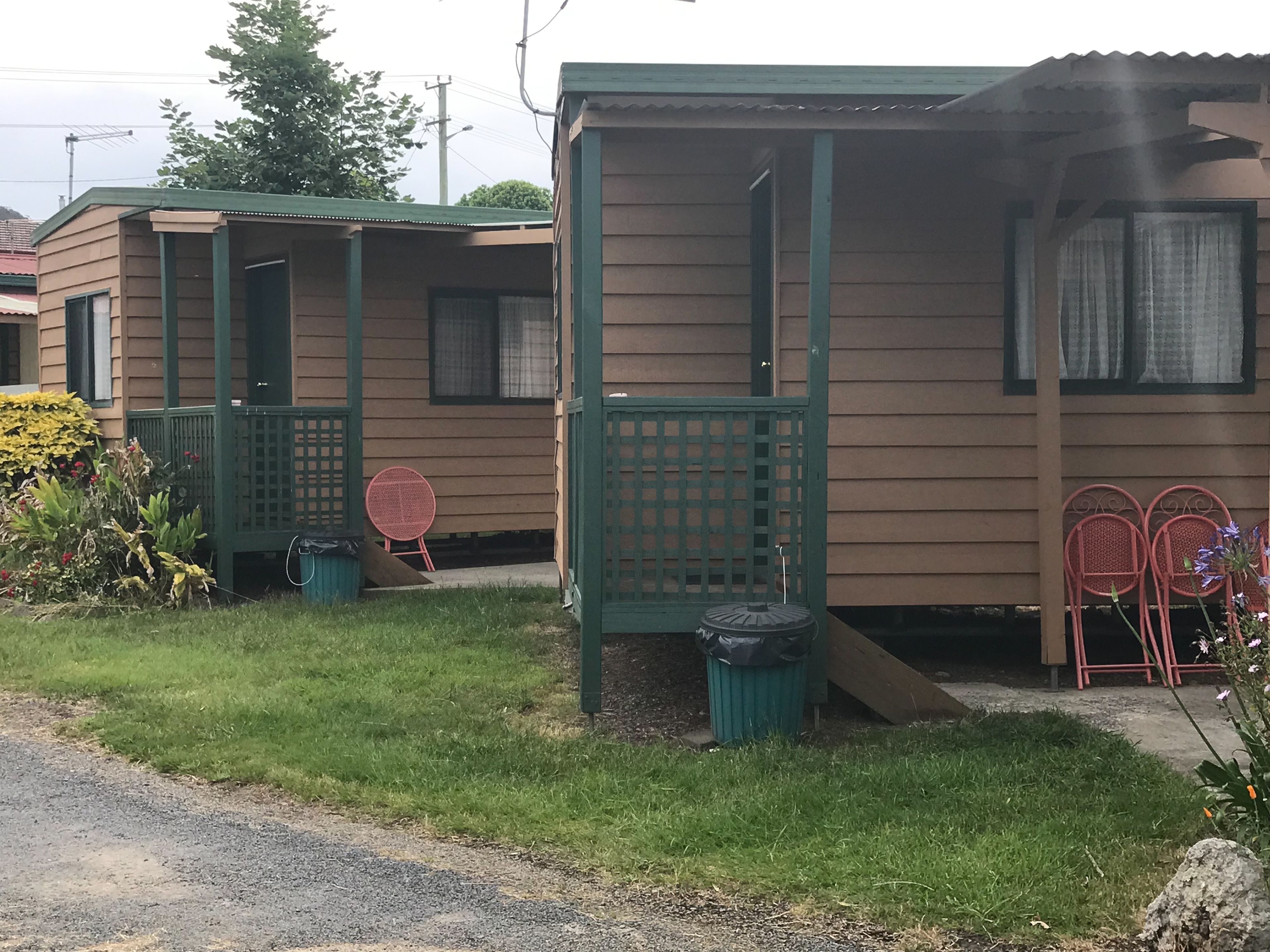 Une rangée de petites cabanes à un seul étage, dotées de balustrades vertes et bordées d’une pelouse.
