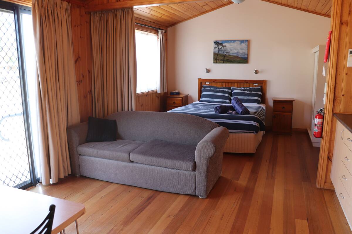 A cozy room with a sofa, a bed with striped bedding, a wooden floor, and a painting on the wall.