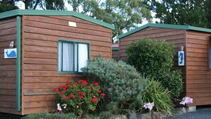 Two wooden cabins with numbers 4 and 3, surrounded by various plants and flowers. - Snug Beach Cabin And Caravan Park (Snug)