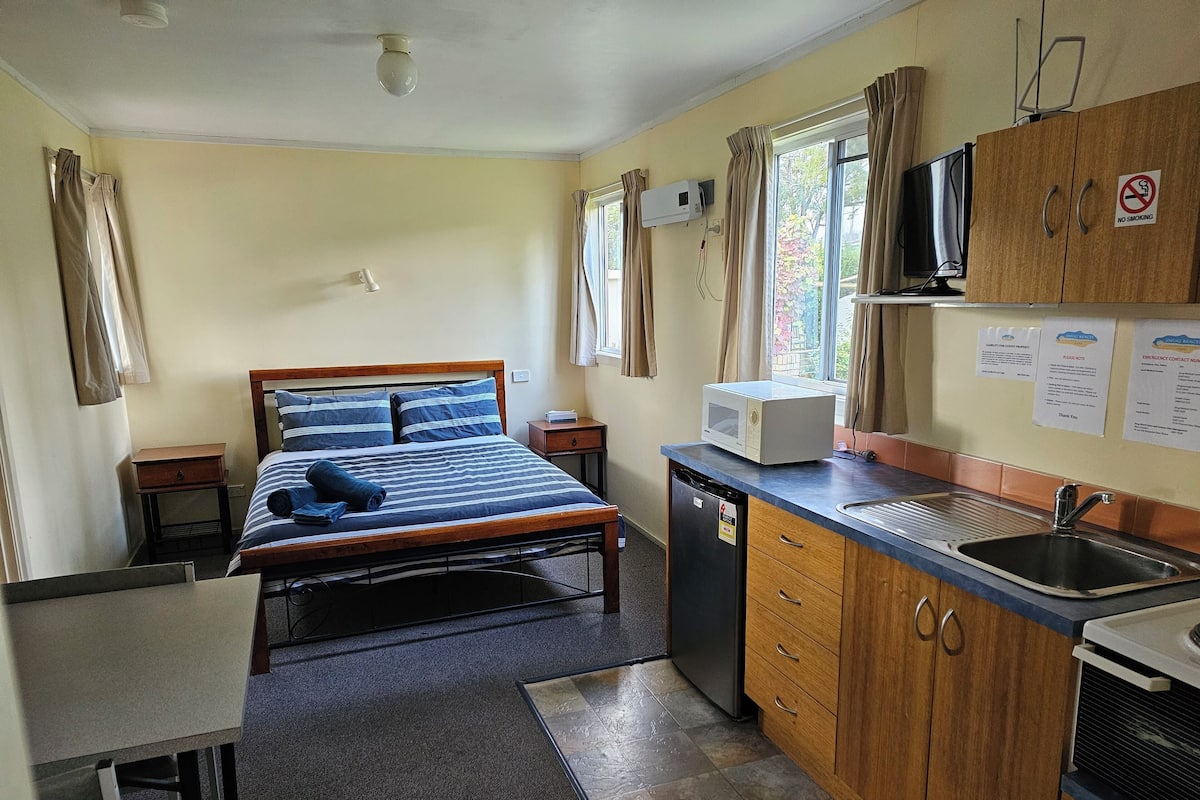 A compact hotel room with a bed, a small desk, a kitchenette, and a bathroom.