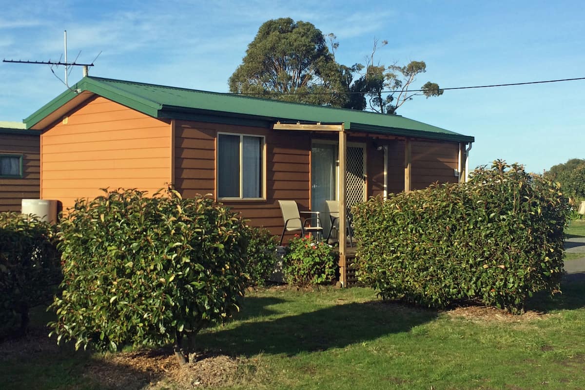 A single-story house with a green roof, a covered porch, and a lawn.