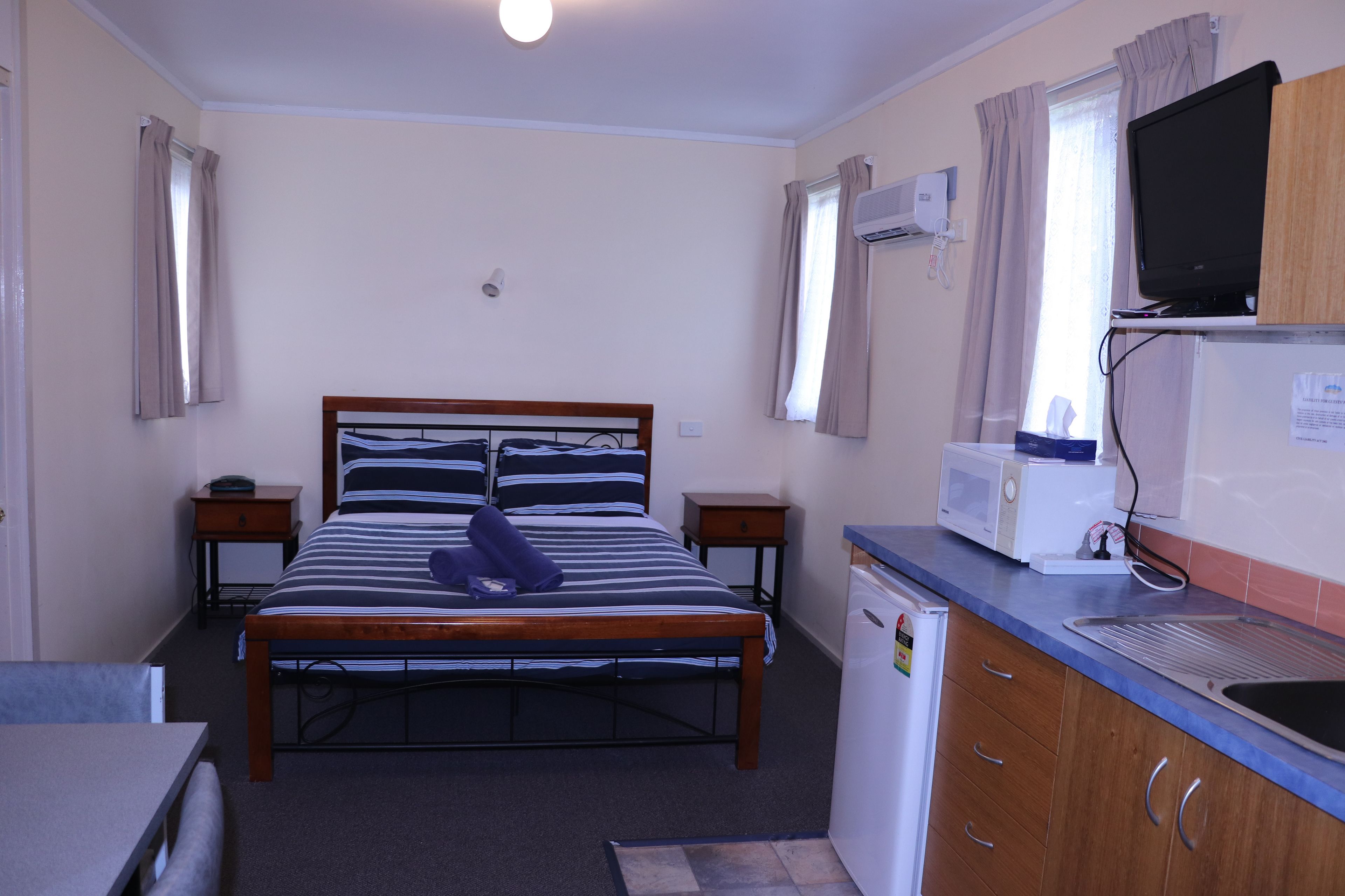 A compact hotel room with a single bed, a small kitchenette, a television, and a window with curtains.
