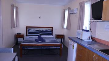 A compact hotel room with a single bed, a small kitchenette, a television, and a window with curtains.