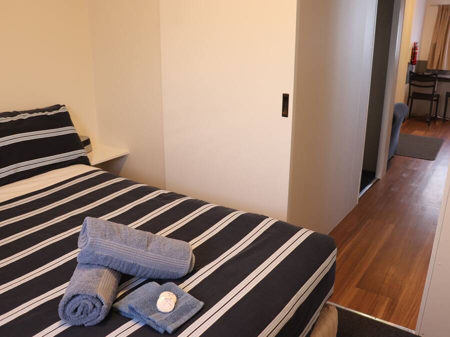 A hotel room with a bed featuring striped bedding, a neatly folded towel, and a small bottle.