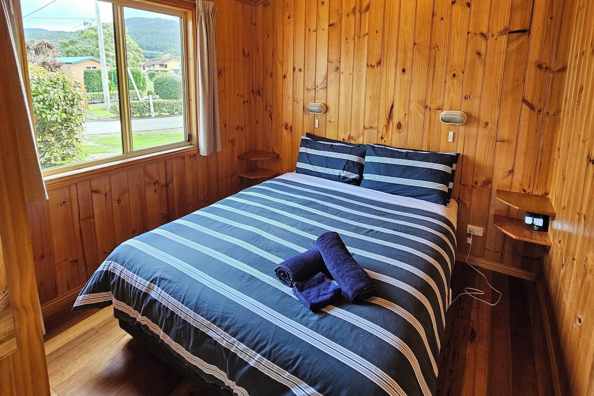 A wooden-paneled room with a bed, a window, and a bedside table.