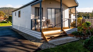 A small, single-story house with a porch and a sliding glass door. - Snug Beach Cabin And Caravan Park (Snug)
