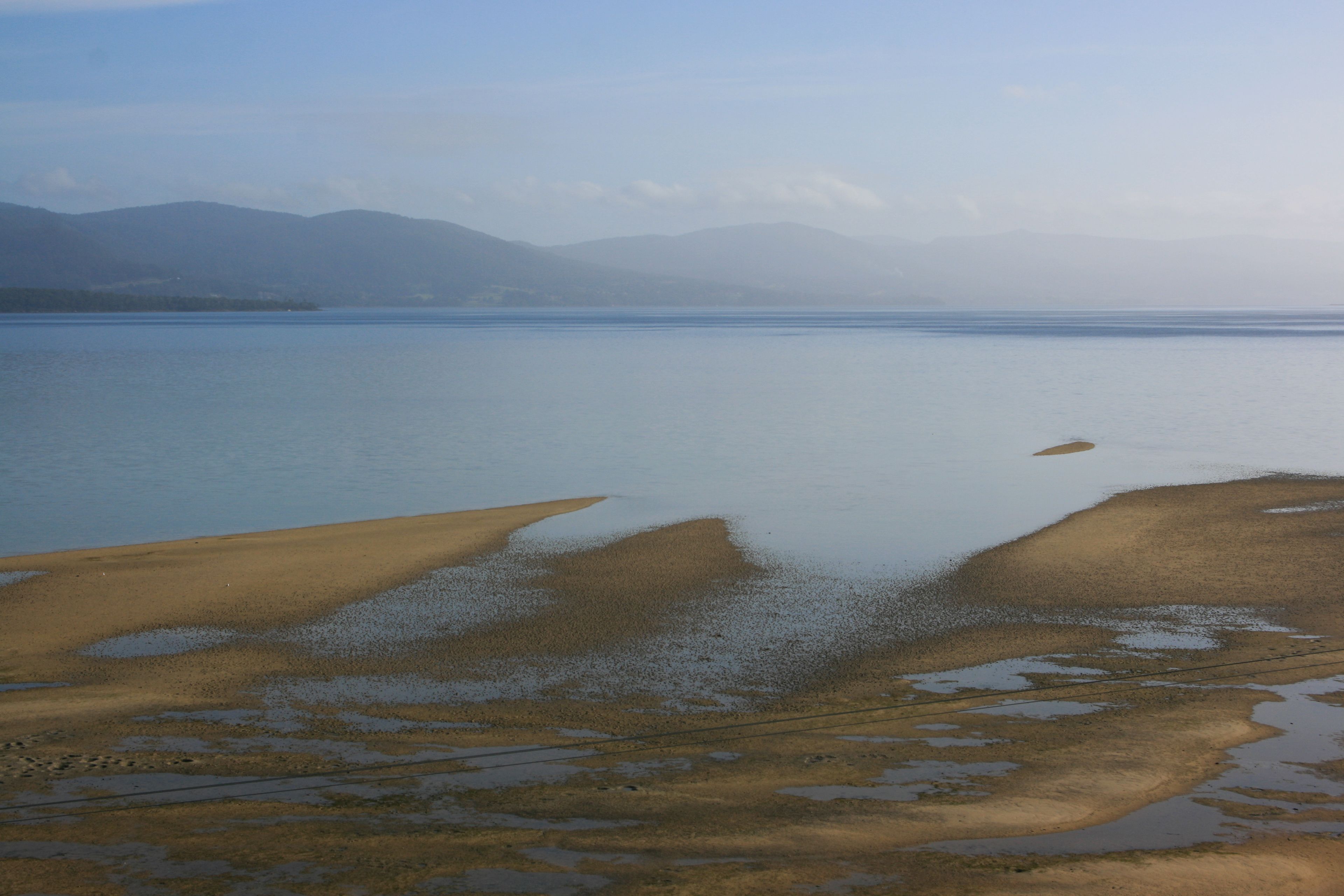A wide view of a lake with a sandy shore and mountains in the background.