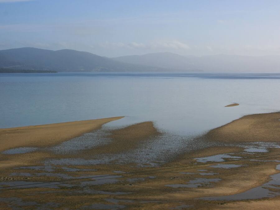 A wide view of a lake with a sandy shore and mountains in the background.