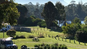 A grassy area with picnic tables, a fenced enclosure, and a vehicle. - Snug Beach Cabin And Caravan Park (Snug)