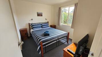 A bedroom with a bed, bedside tables, a desk with a television, a window with curtains, and a door.