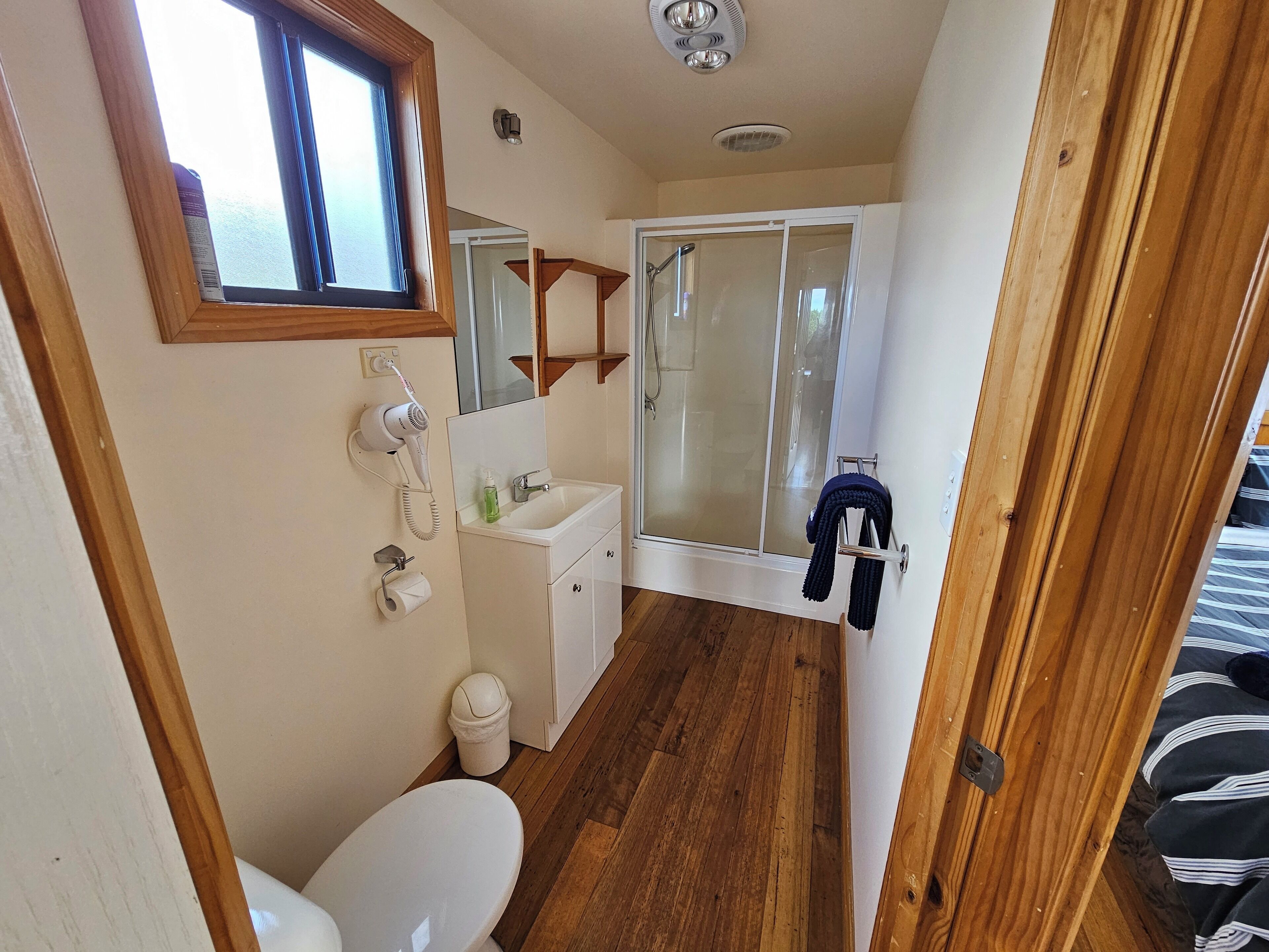 A compact bathroom with a toilet, a sink, a hairdryer, and a shower with a glass door.
