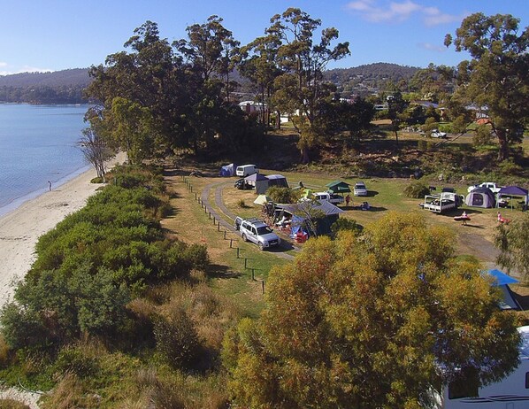 Un camping con vehículos recreativos y tiendas de campaña, una playa y colinas al fondo.