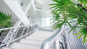 A spiral staircase with white railings and a metal handrail, surrounded by green plants. - Baan Yamoo Ranong (Ranong)