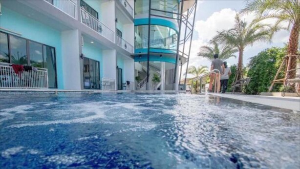 A swimming pool with a clear view of the surrounding hotel architecture, including balconies and a glass elevator. - Baan Yamoo Ranong (Ranong)