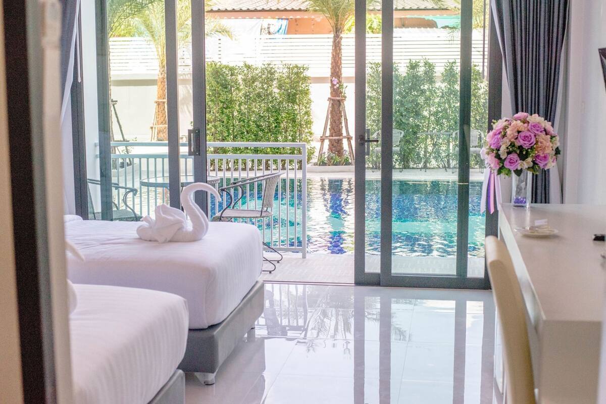 A hotel room with two beds, a balcony with a pool, and a view of the outdoors.