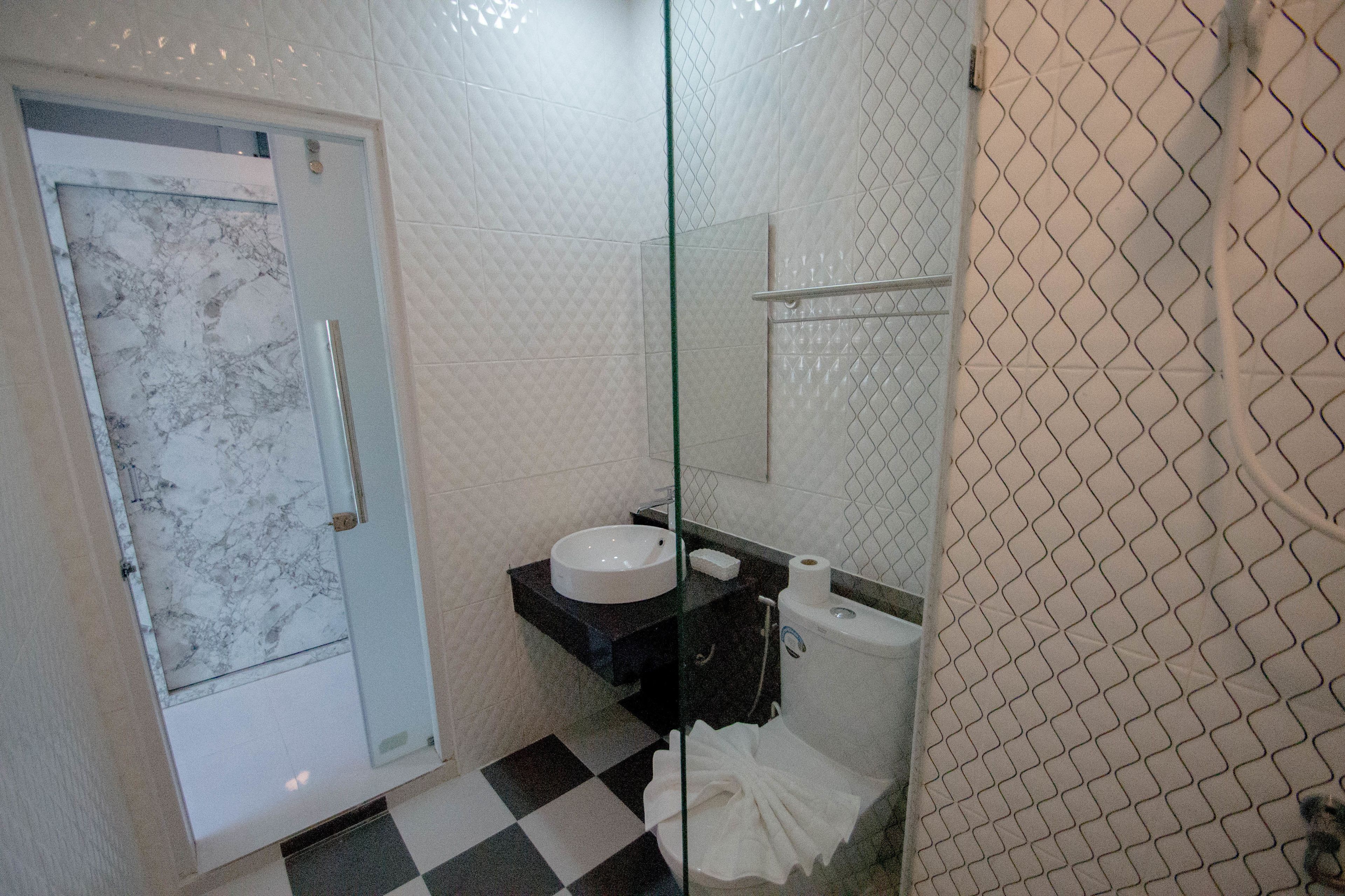 Une salle de bain dotée d’une douche à parois de verre, d’une porte de douche recouverte de carreaux de marbre, d’un plan de toilette noir avec un évier, de toilettes et d’un porte-serviettes.