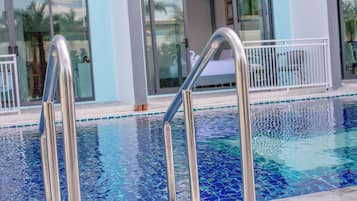 A swimming pool with clear blue water, metal pool ladders, and a white railing.