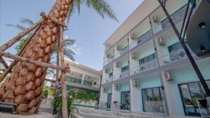 A multi-story hotel with balconies, air conditioning units, and a palm tree in the foreground. - Baan Yamoo Ranong (Ranong)